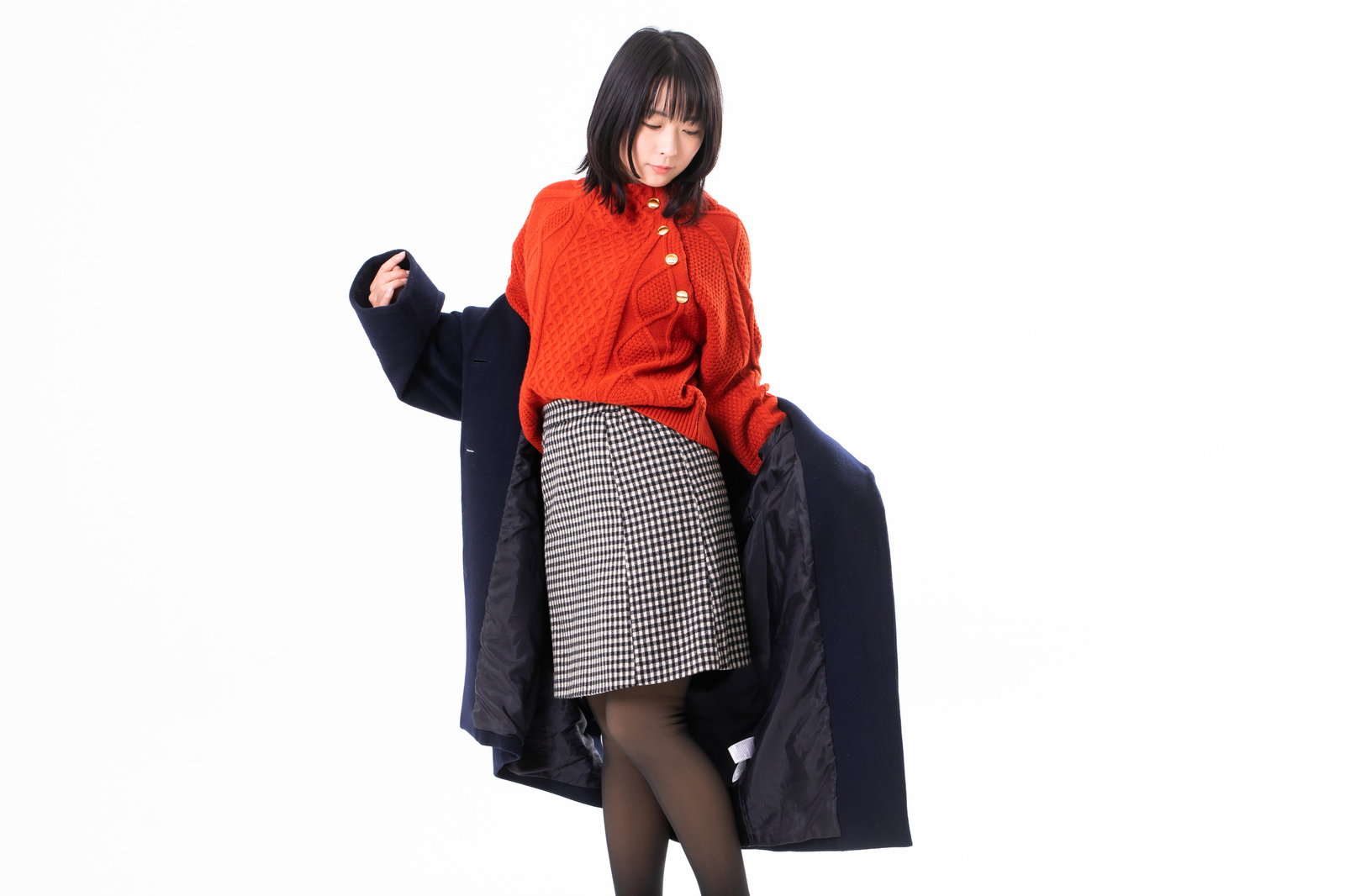 黒いコートに袖を通している赤いニットを着た女性［モデル：にゃるる］