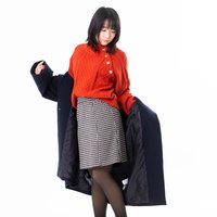 赤いニットに黒いコートを羽織り袖を通す女性の写真