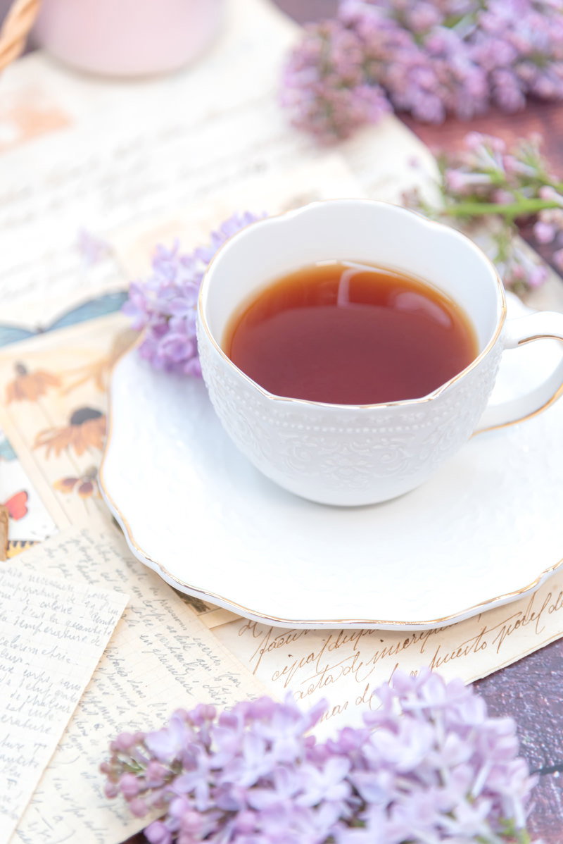 白いティーカップに入った紅茶と紫のライラックの花が配置されたテーブル
