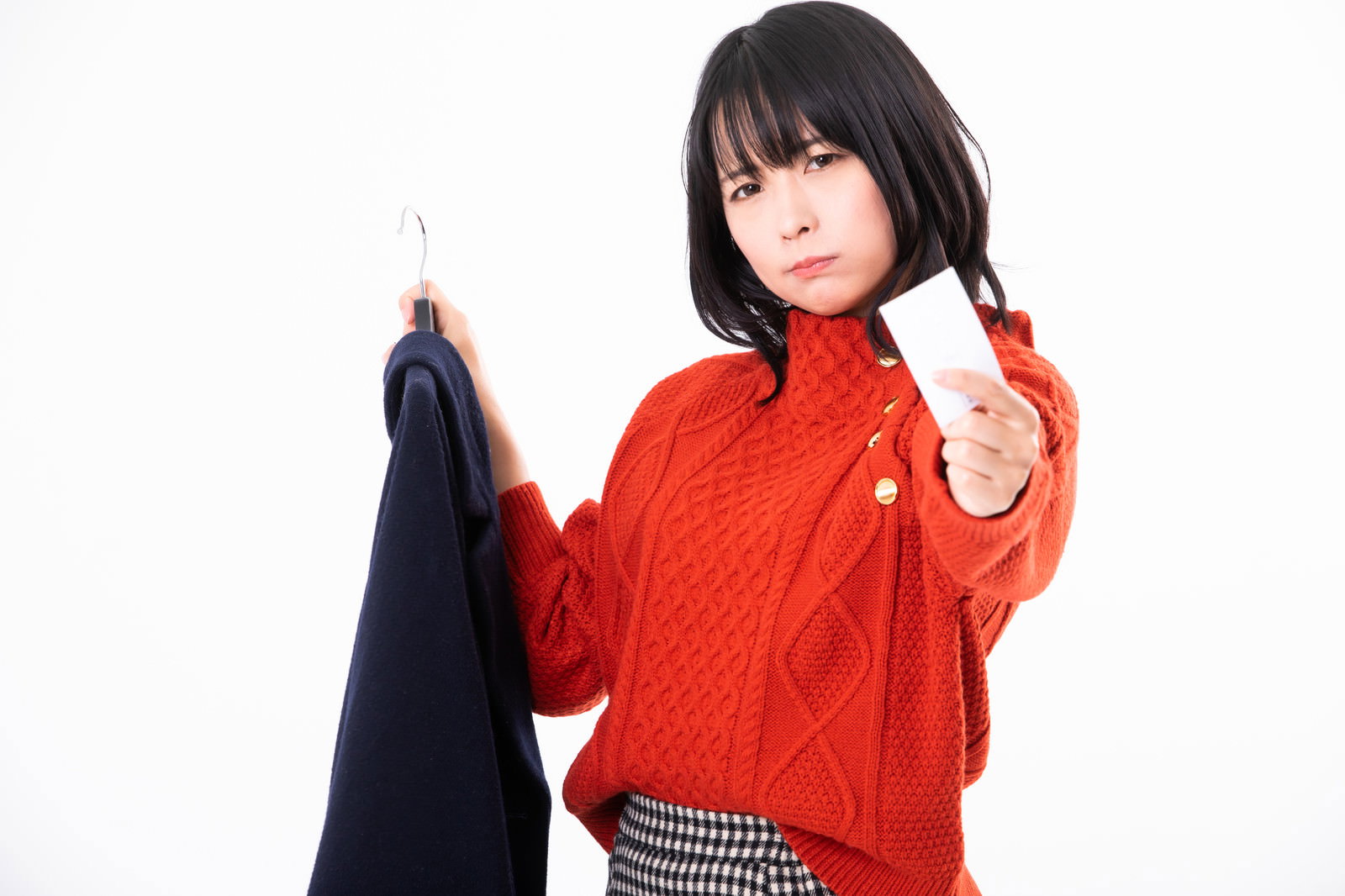 赤いニットの女性がコートと名刺を持ち怒った表情を見せている［モデル：にゃるる］