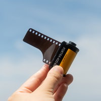 35mmフィルムを指で摘んで掲げる手と青空の写真
