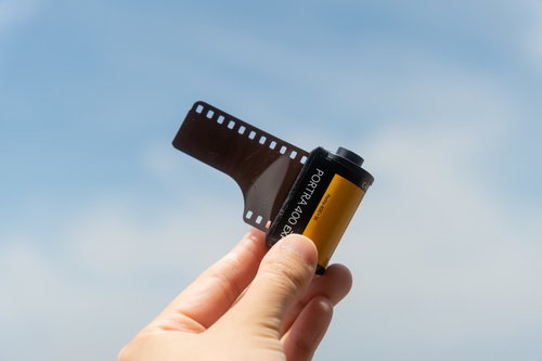 35mmフィルムを指で摘んで掲げる手と青空
