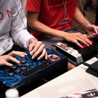 アケコンを持って隣同士で対戦ゲームをプレイする男性たちの写真