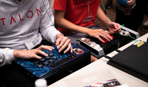 アケコンを持って隣同士で対戦ゲームをプレイする男性たち