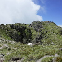 晴天の日光白根山山頂周辺の岩場と緑、遠方の山々を望む景観の写真