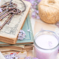 キャンドルと洋書に寄り添う紫のライラックの写真