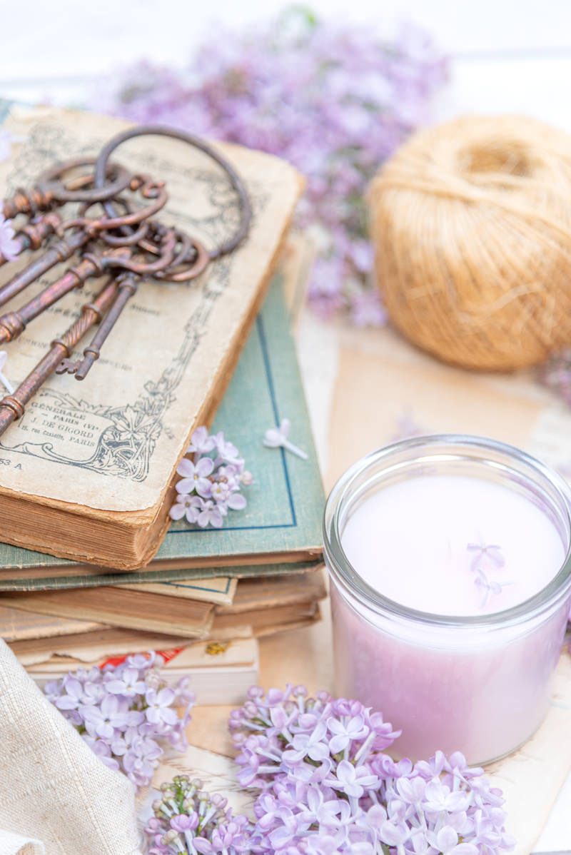 洋書の上にライラックの花が置かれ、キャンドルと古い鍵が配置された写真