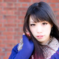 赤レンガの壁の前で髪をかきあげるポーズの女性の写真