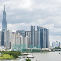 サイゴン川沿いに立つビル群と川岸の緑地、対岸の都市景観の写真