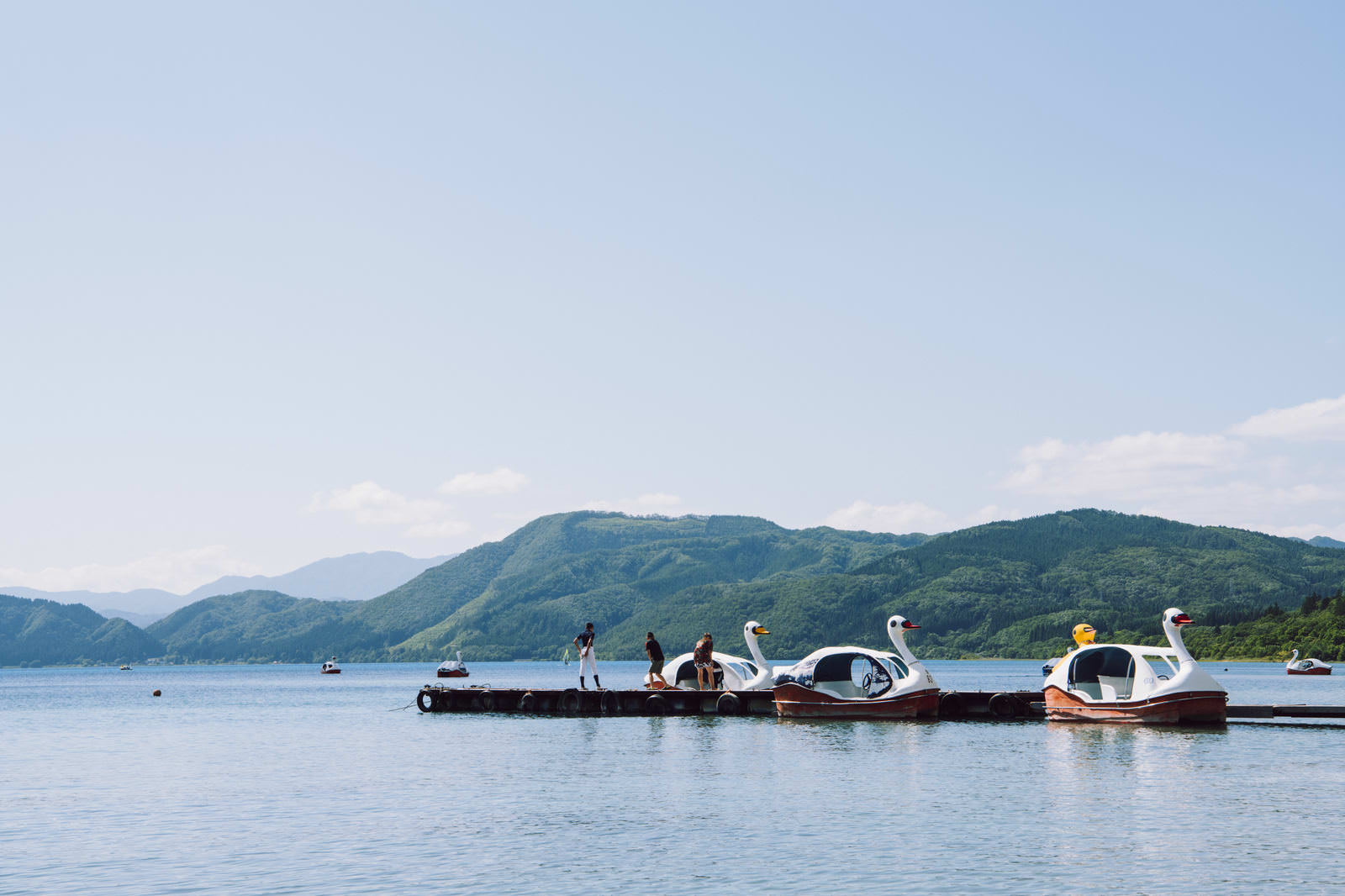 湖の桟橋に白いスワンボートが係留され若者たちが立っている風景