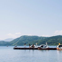 湖面に浮かぶ白いスワンボートと桟橋の若者たちの写真