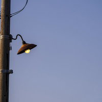 電柱の古びた外灯に止まるカラス、青空を背景にの写真