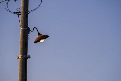 電柱の古びた外灯に止まるカラス、青空を背景に