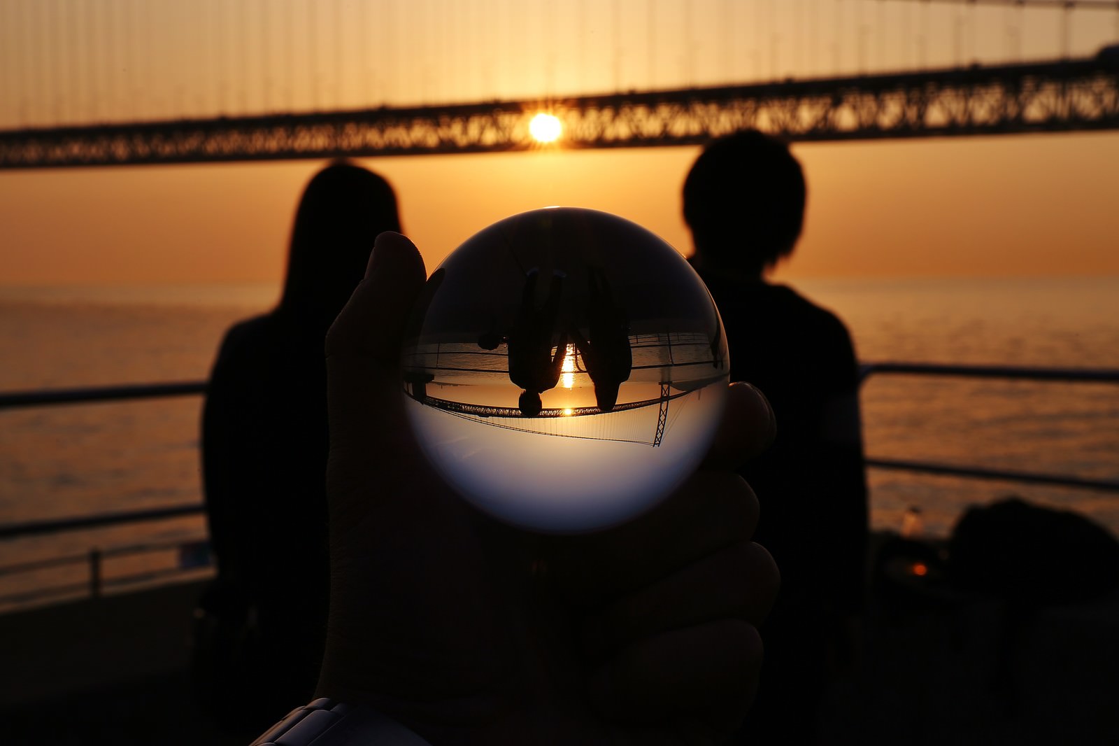 夕日を背景に橋の上で寄り添うカップルのシルエットが水晶玉に映る