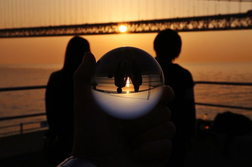 夕暮れの橋で寄り添う恋人と水晶玉に映る二人のシルエット