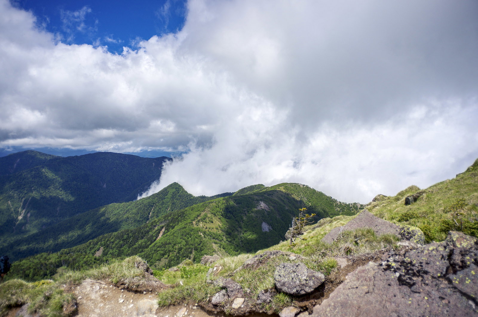 青空と雲が流れる奥日光の山々と手前の岩場