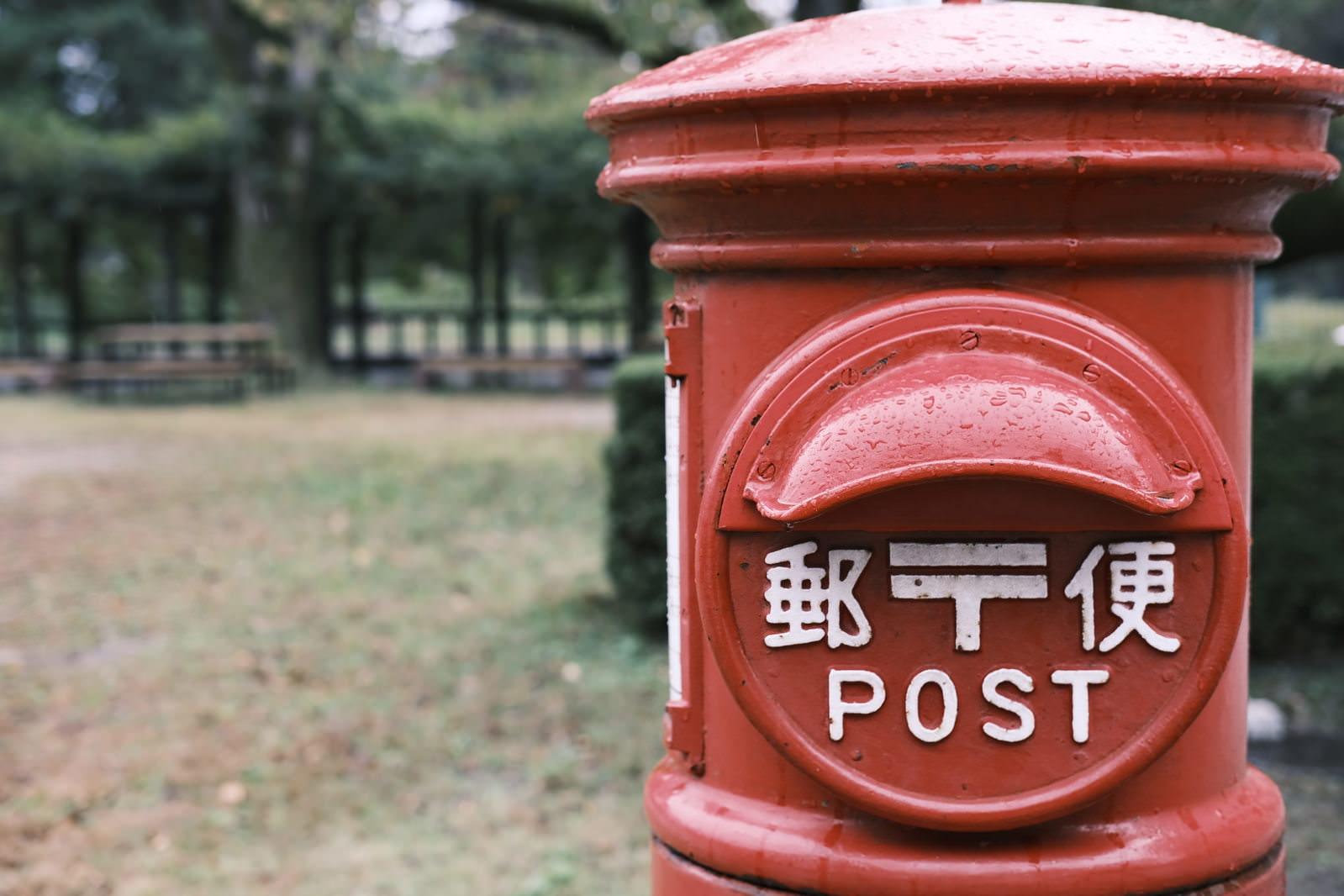 公園に立つ雨粒のついた赤い丸型郵便ポスト
