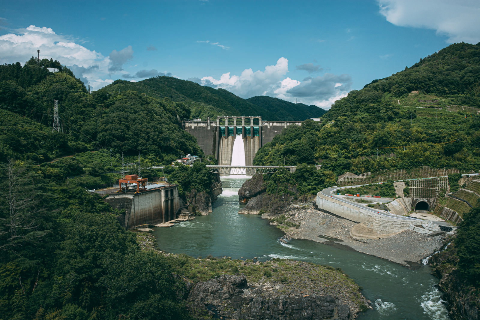緑の山々に囲まれた丸山ダムと流れ出る川の風景