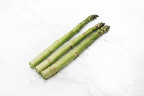 白いテーブルに並べたアスパラガスの3本と調理