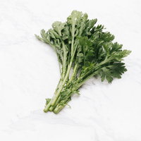 白いテーブルに置いた春菊の束のの写真