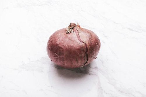 赤玉ねぎの新鮮な一個、採れたての食材、白い大理石の上に置かれた球形の野菜