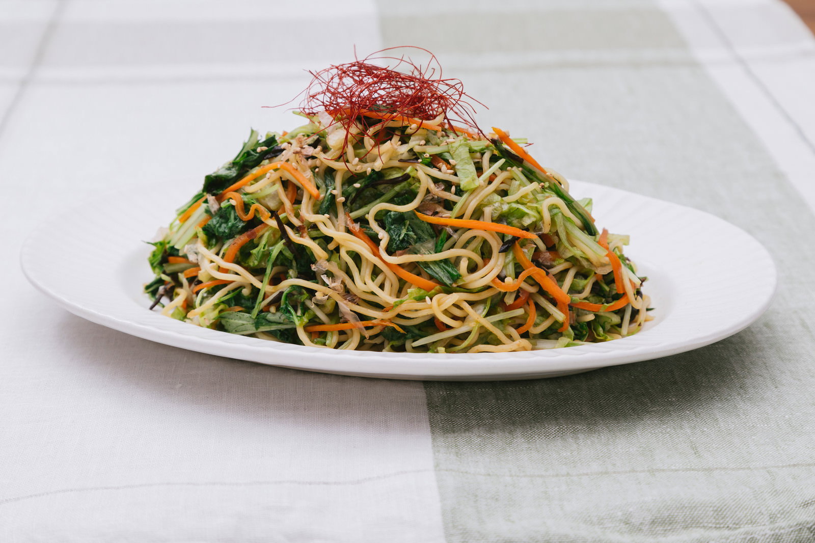 白い皿に盛られた野菜たっぷりの焼きそば。ほうれん草、もやし、人参、玉ねぎが混ぜ込まれ、赤い装飾が頂上に立てられている。