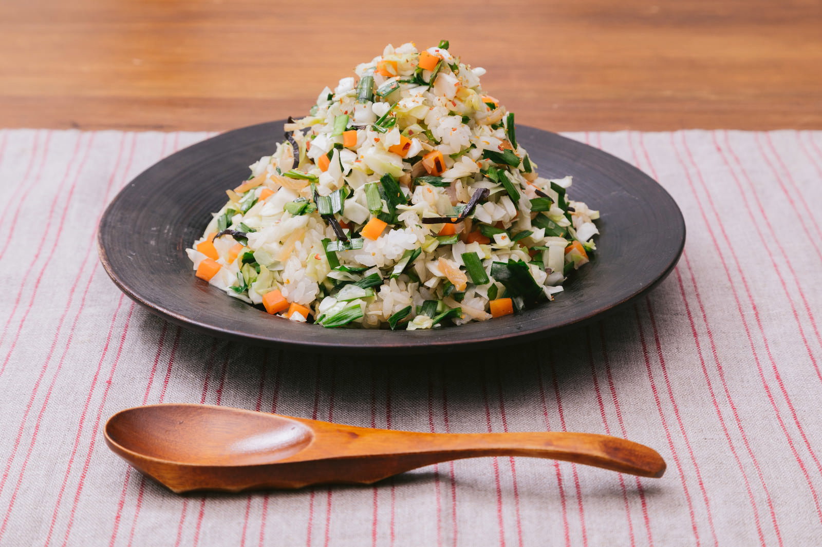 黒い皿に盛られた野菜入りチャーハン。ネギとニンジンの彩りが混ざったボリュームのある一皿
