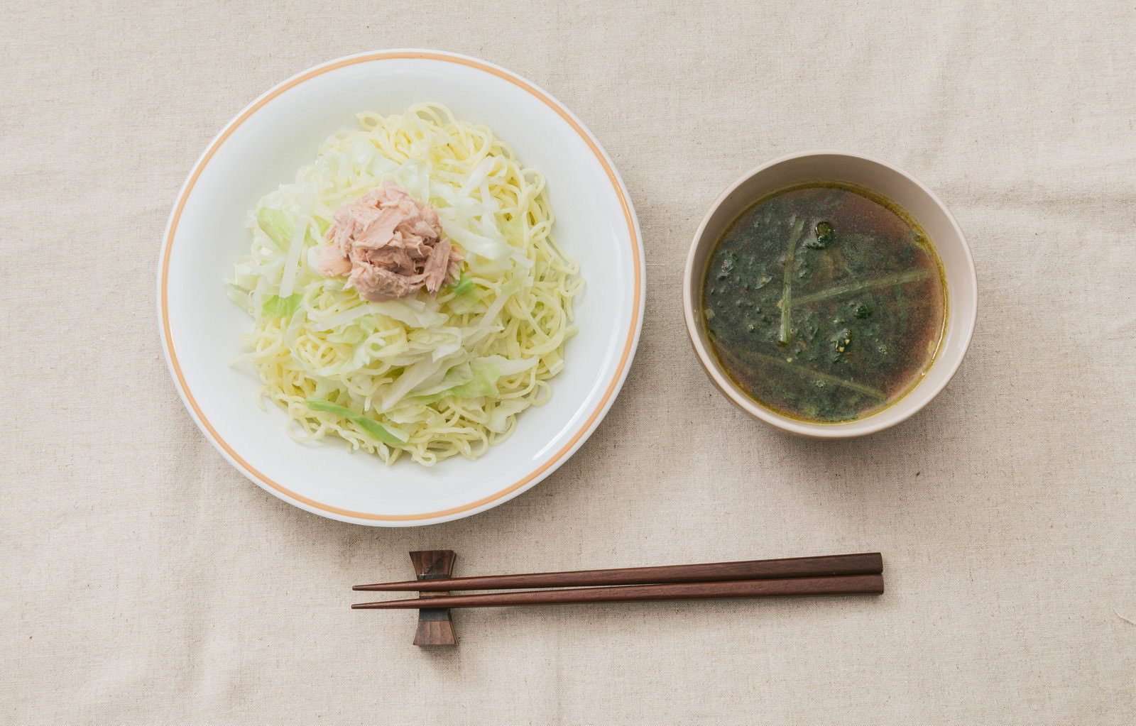 白い皿のつけ麺、隣に緑色のスープ、木製の箸が添えられた食事