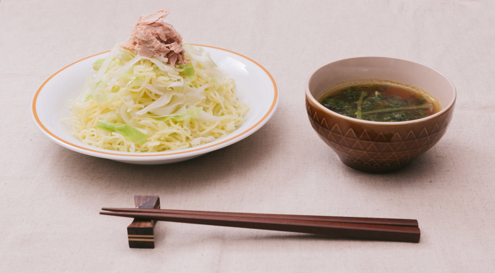 白い縁取りの器に盛られた黄色い麺の上に茶色い牛肉をのせ、隣に茶色い丼のカレーつけ汁と木製箸を配置した食卓