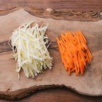 木製まな板の上で千切りにしたキャベツとにんじんの写真