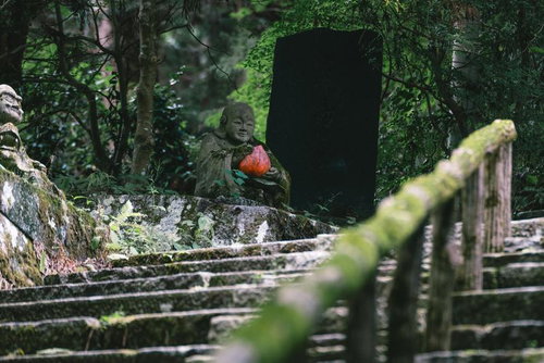 緑に包まれた石段の上で赤い果実を持つ羅漢像