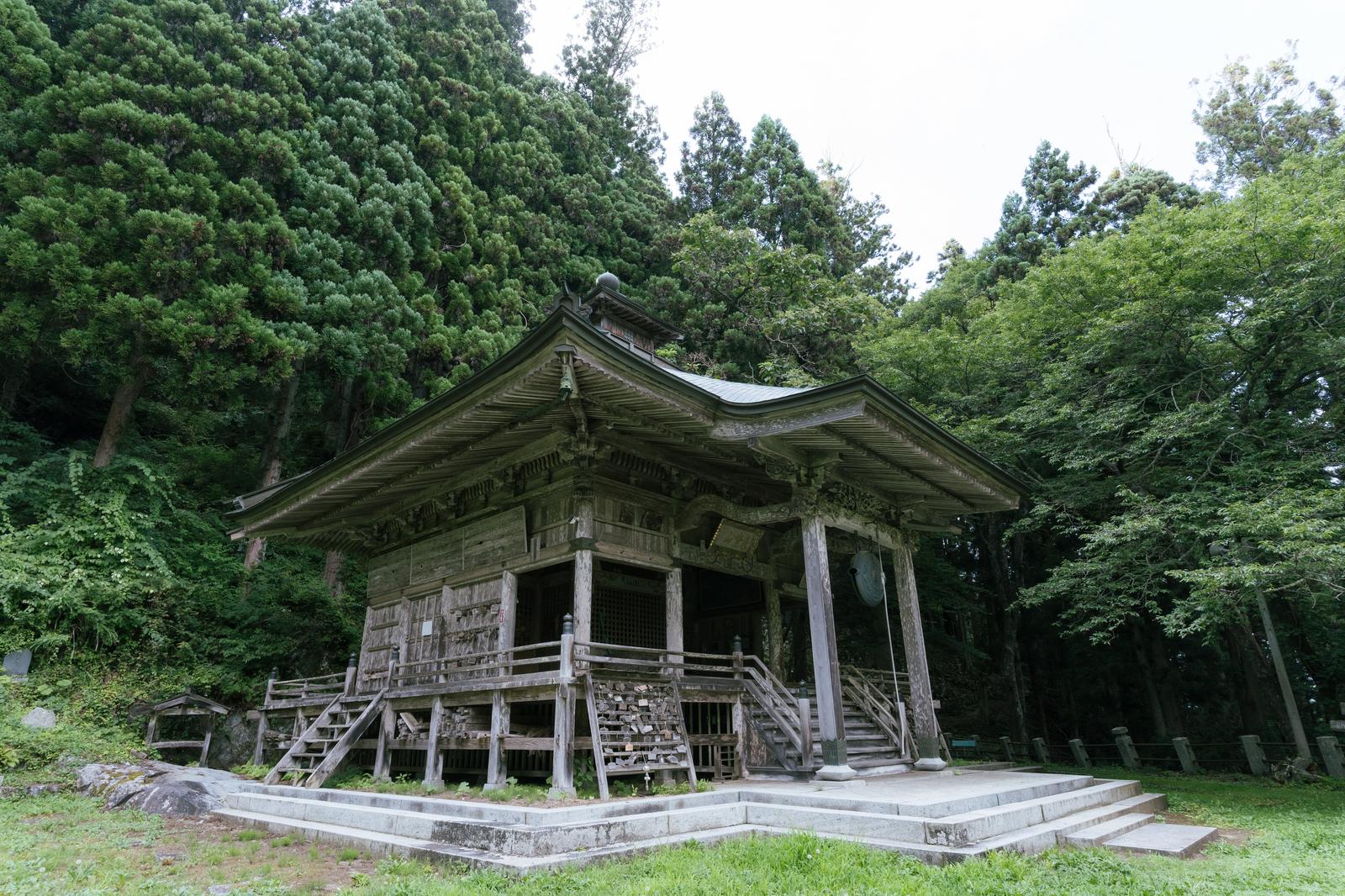 杉の樹林に囲まれた木造の観音堂。石製基壇の上に建つ古い寺院建築