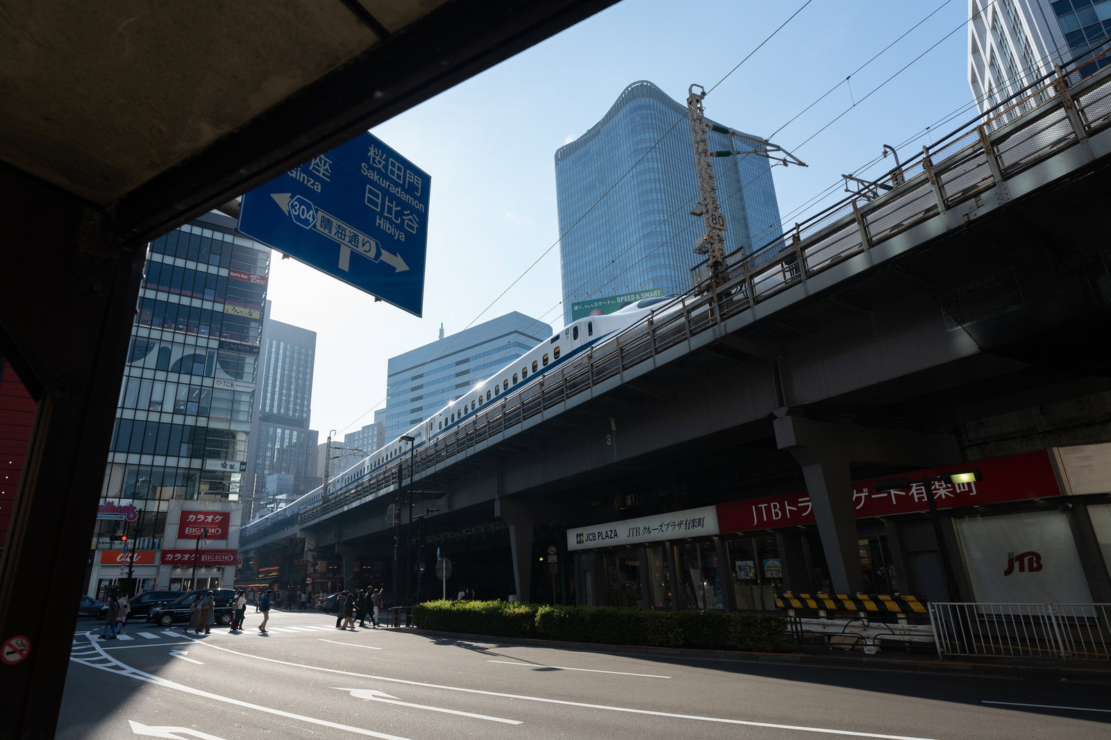 有楽町駅前の架線下を走る新幹線と周辺ビル群の風景