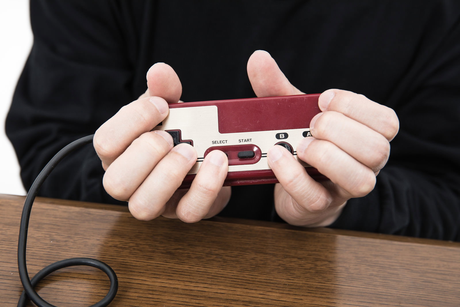 ファミコンのコントローラーを独特な持ち方で握る手元［モデル：大川竜弥］