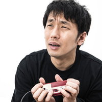 こんなコントローラーの持ち方じゃうまくプレイできないと涙目のゲーマー男性の写真