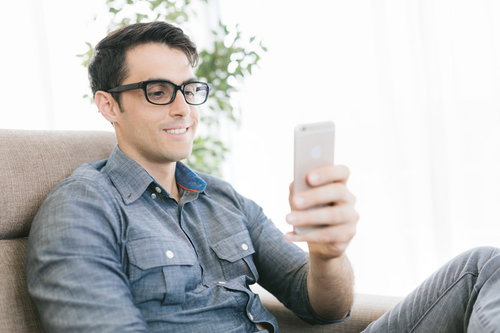 ソファーでスマホを見てニヤニヤする眼鏡の男性