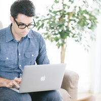 自宅のソファでノートパソコンを操作するエンジニア男性の写真