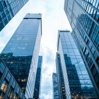 見上げたガラス張りの高層ビル群の写真