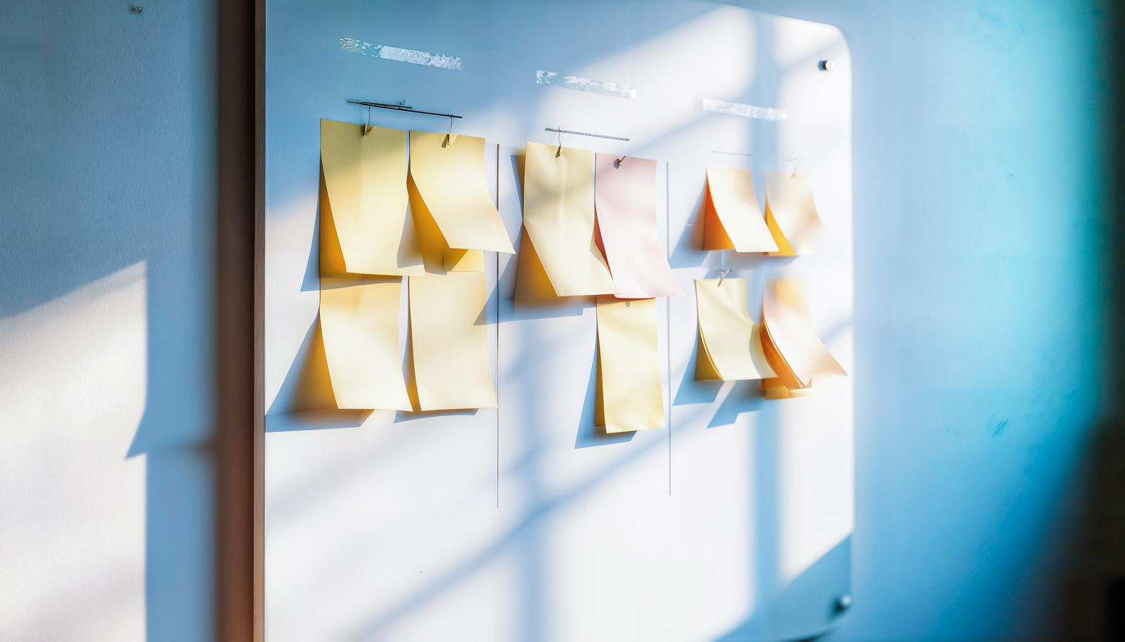 Multiple sticky note memos held in place by clips on a whiteboard with natural light streaming in from a window
