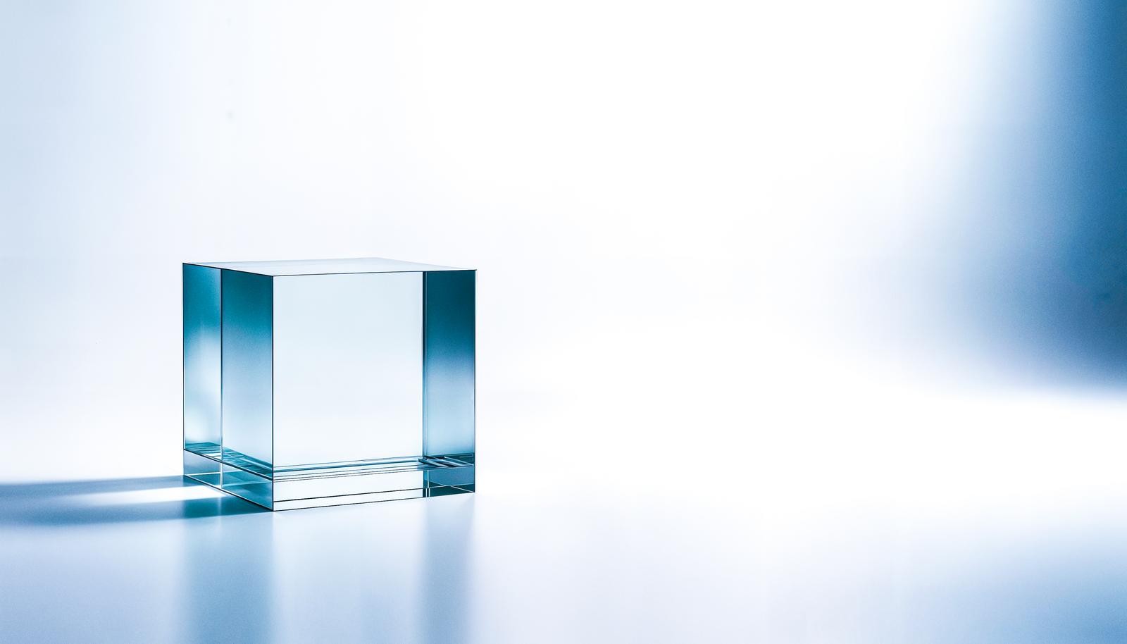 A single transparent acrylic cube placed on a white background, with subtle blue light