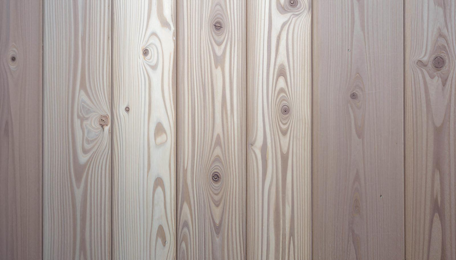 A whitish wooden board wall with boards arranged vertically. The knots and wood grain patterns are clearly visible.