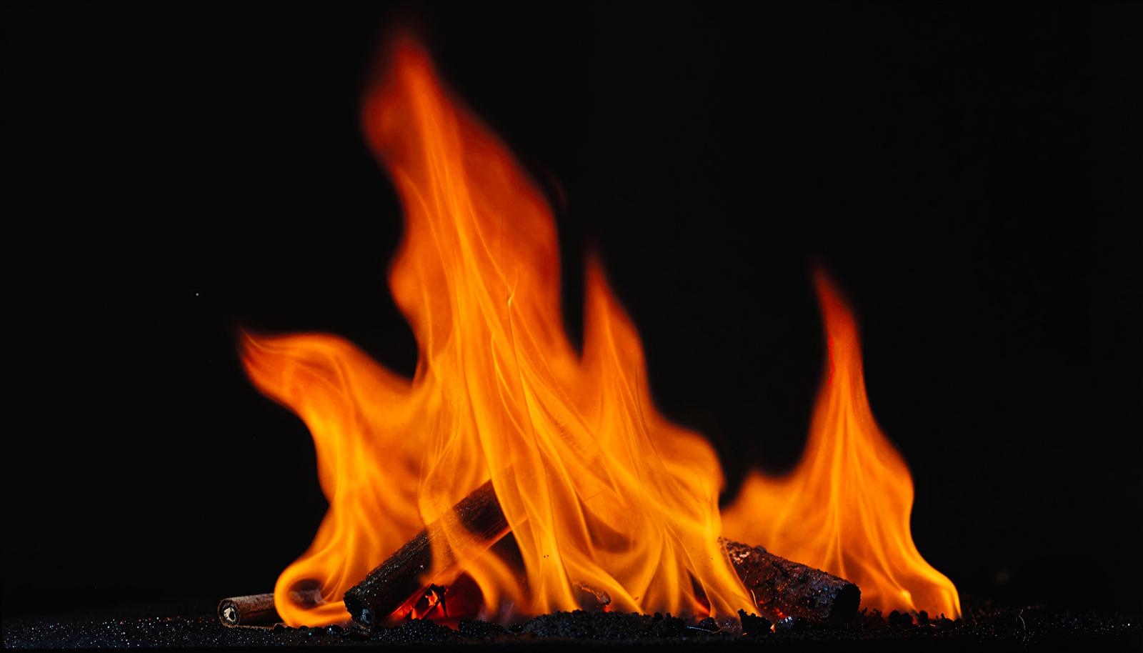 Blazing flames rising over firewood with red embers