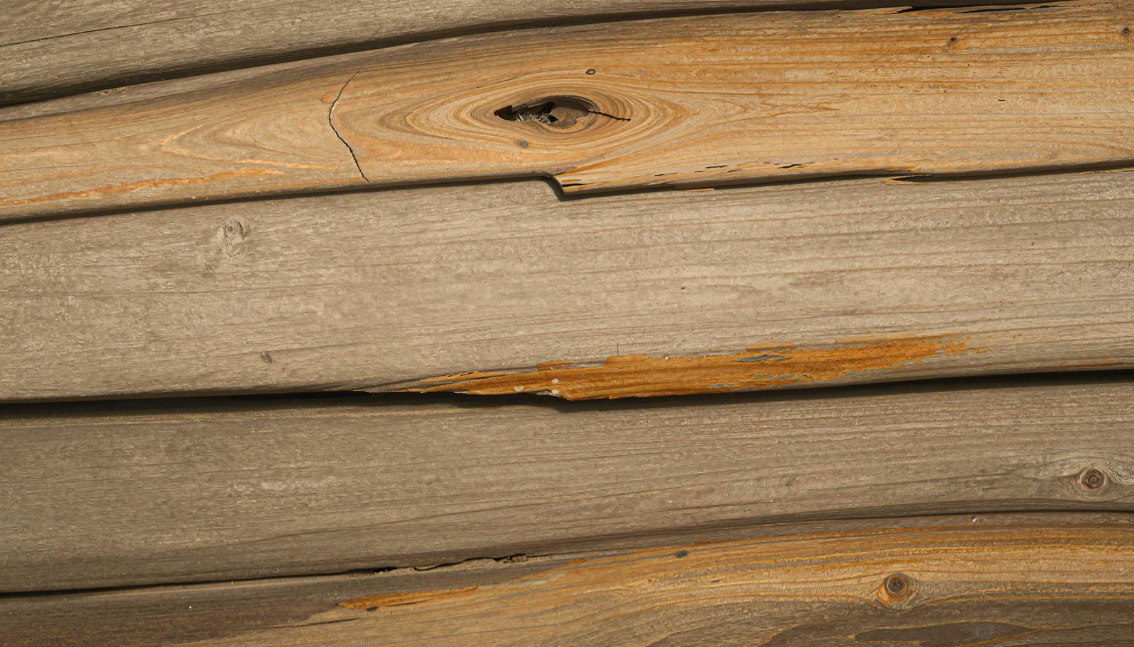 横に重なった古い木材の板に節穴とささくれが見えるAI画像