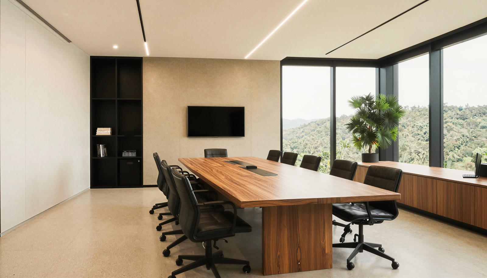 木製の長テーブルと黒い革張りチェアが並ぶ会議室。窓の外には山の緑が広がる