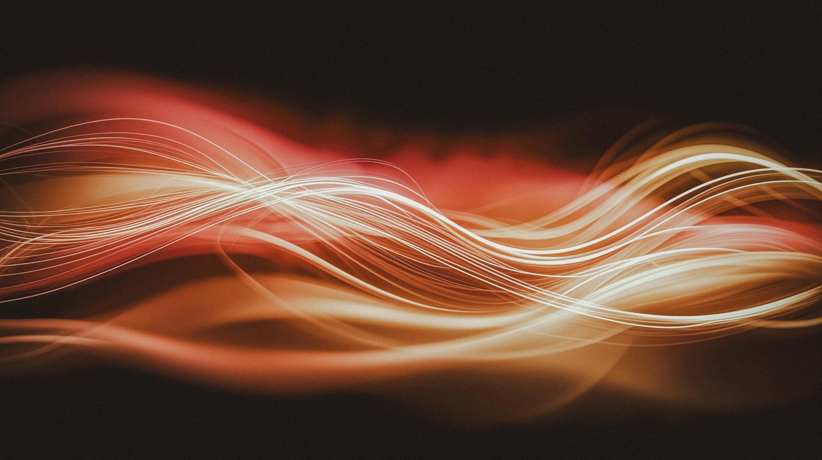 暗い背景にオレンジ色の光が波状に流れる抽象的なCG画像