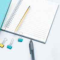 白を基調としたデスクに開かれたノートとペンの写真