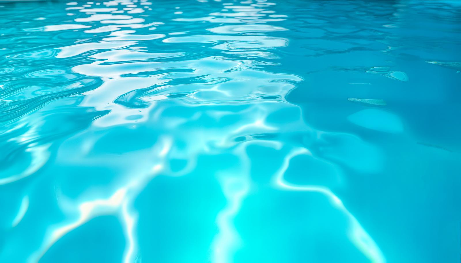 光を反射して波紋が広がる青いプールの水面のクローズアップ