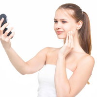 コンパクトミラーを見ながらスキンケアする女性の写真