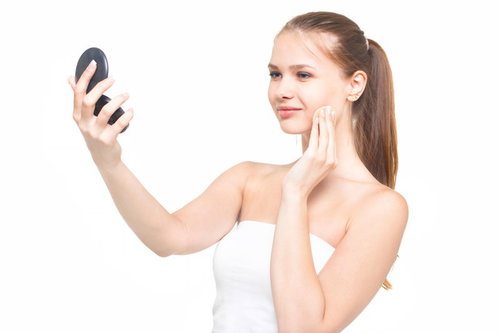 コンパクトミラーを見ながらスキンケアする女性