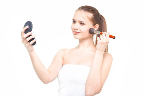 コンパクトミラーを持ちながらチークブラシでメイクする外国人女性